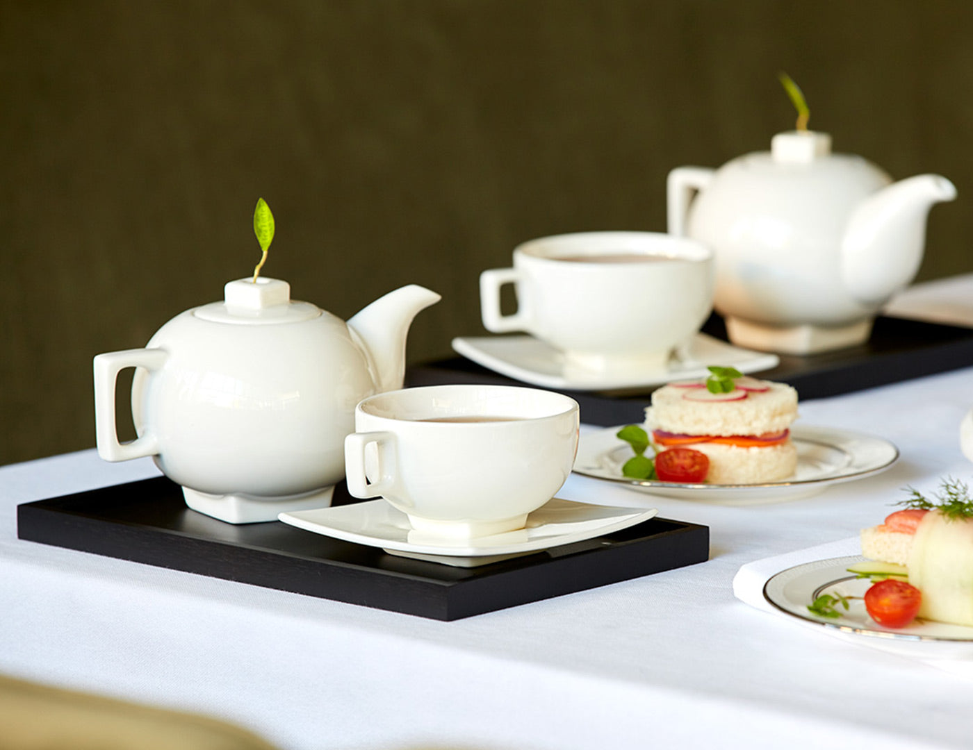 Solstice teapot and teacup on a black tray with desserts on a dining table