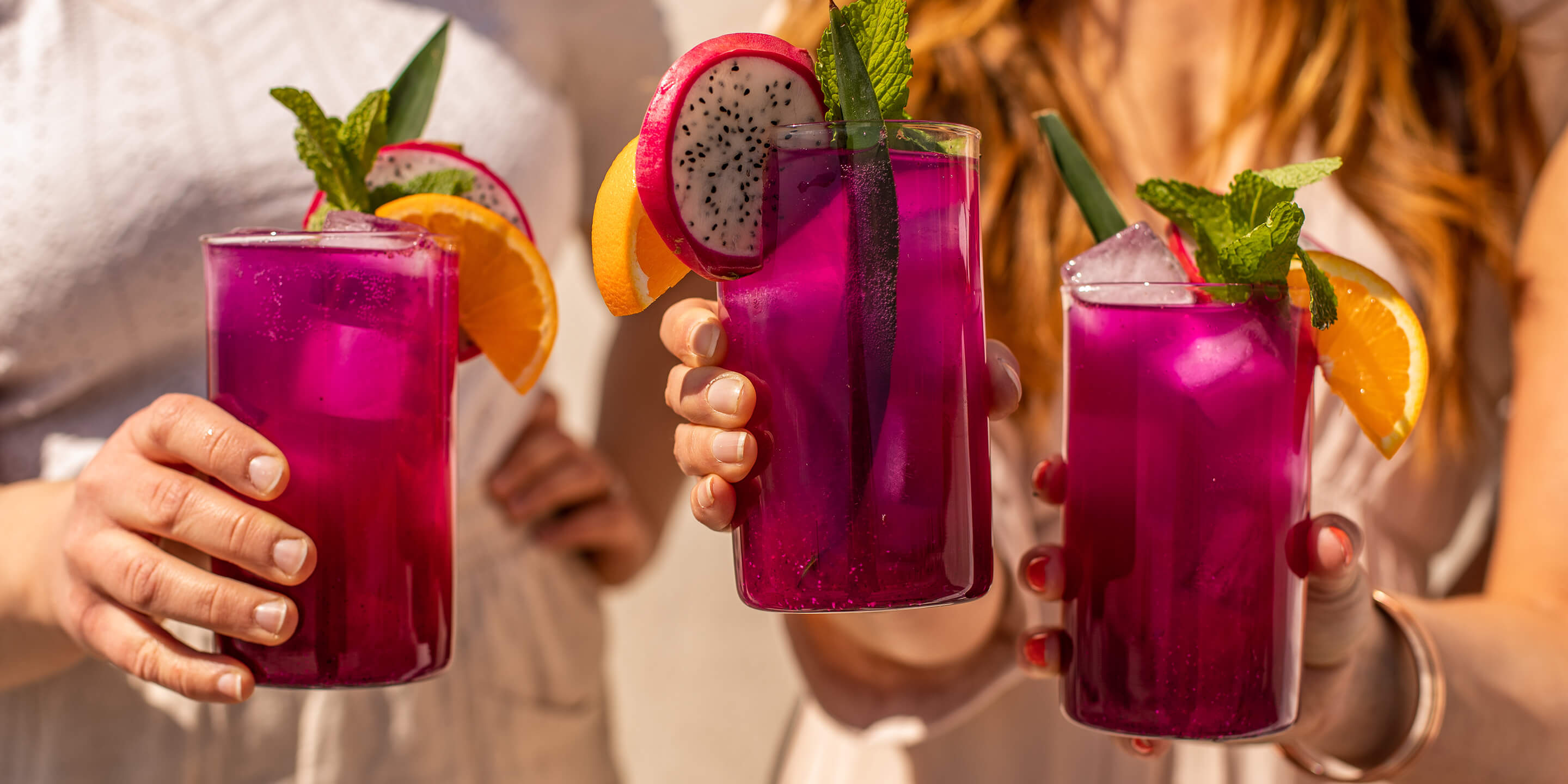 Three glasses of blue mint dragonfruit lemonade being held in the air