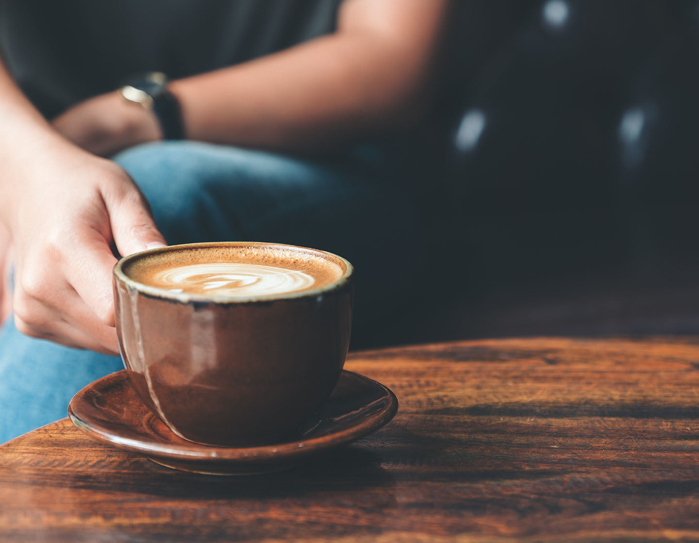 Picking up a latte in a brown ceramic mug at a cafe