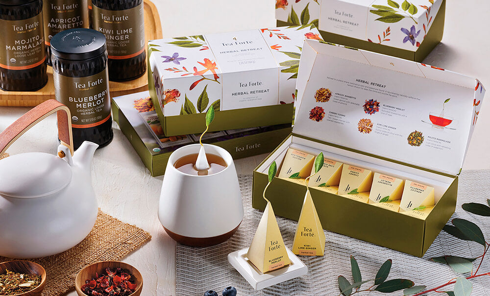 Herbal Retreat tea assortment in a 10 and 20 count presentation box on table with teacups, teapot and loose leaf tea.