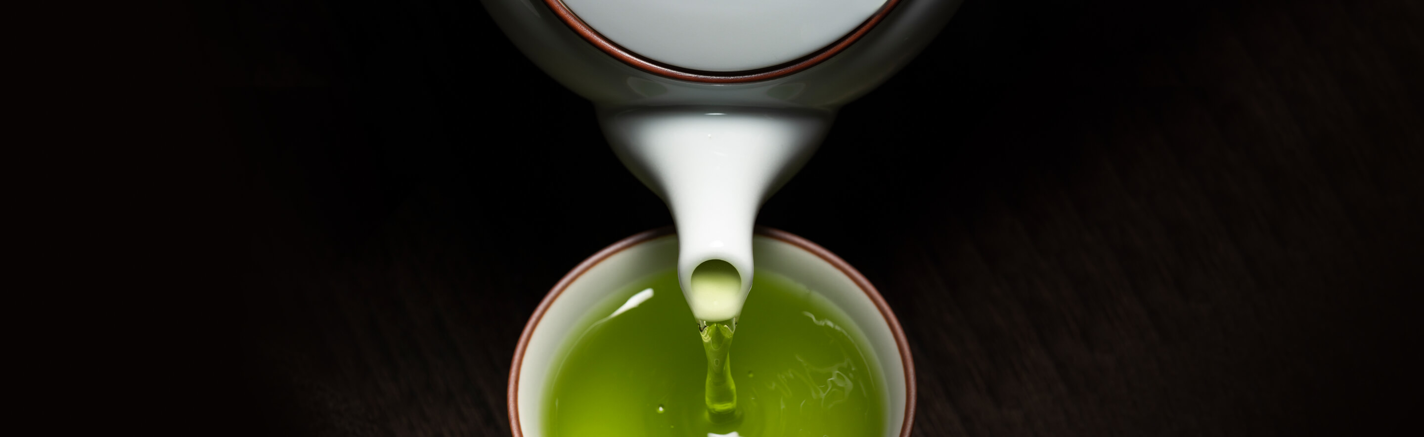 Green tea being poured into a white teacup from a white teapot