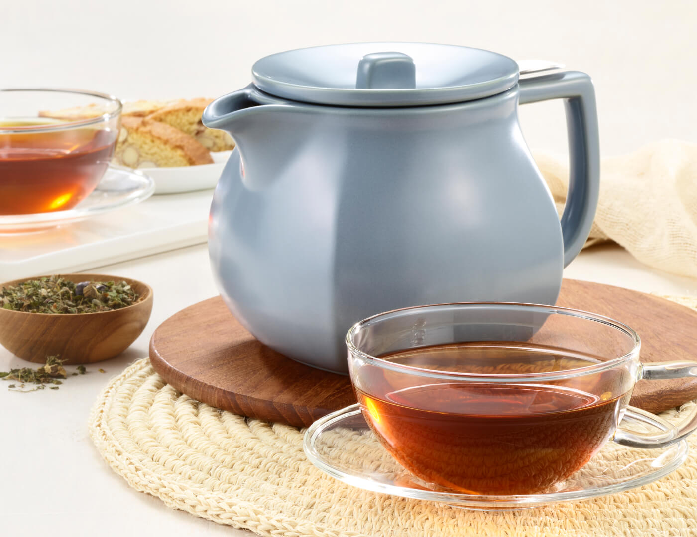 Fiore Stone Blue Teapot on a table with a glass cup of tea and loose tea