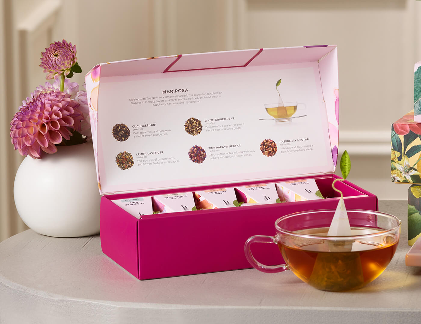 Mariposa Petite Presentation Box of 10 pyramid tea infusers, open on a table with a glass cup of tea