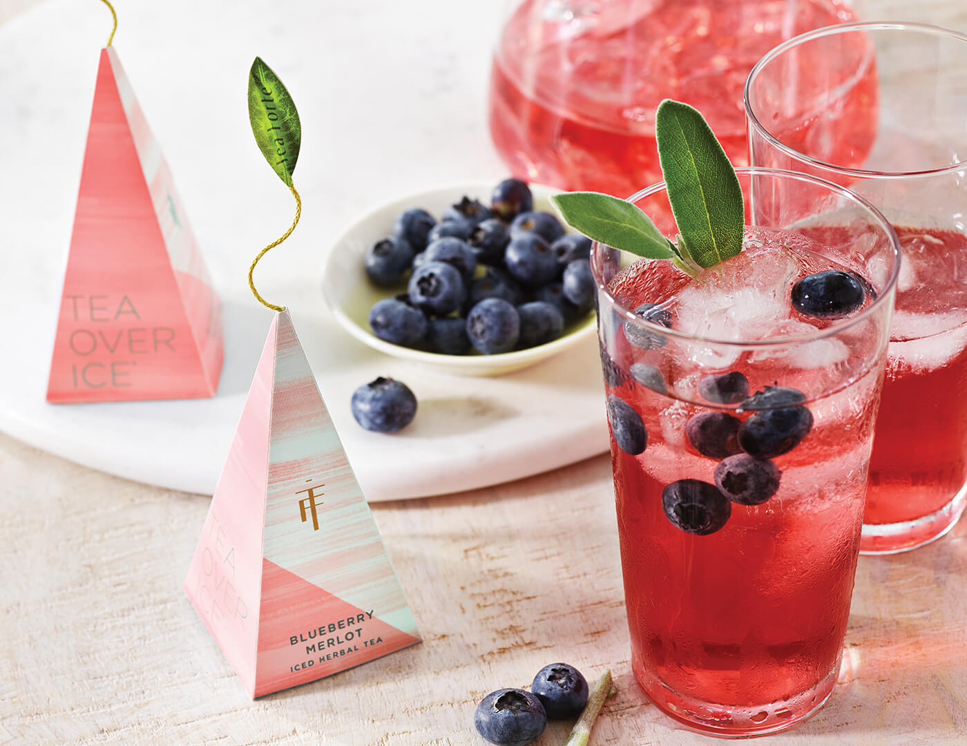 Glass of Raspbery Nectar Tea Over Ice with blueberries and pyramid infuser.