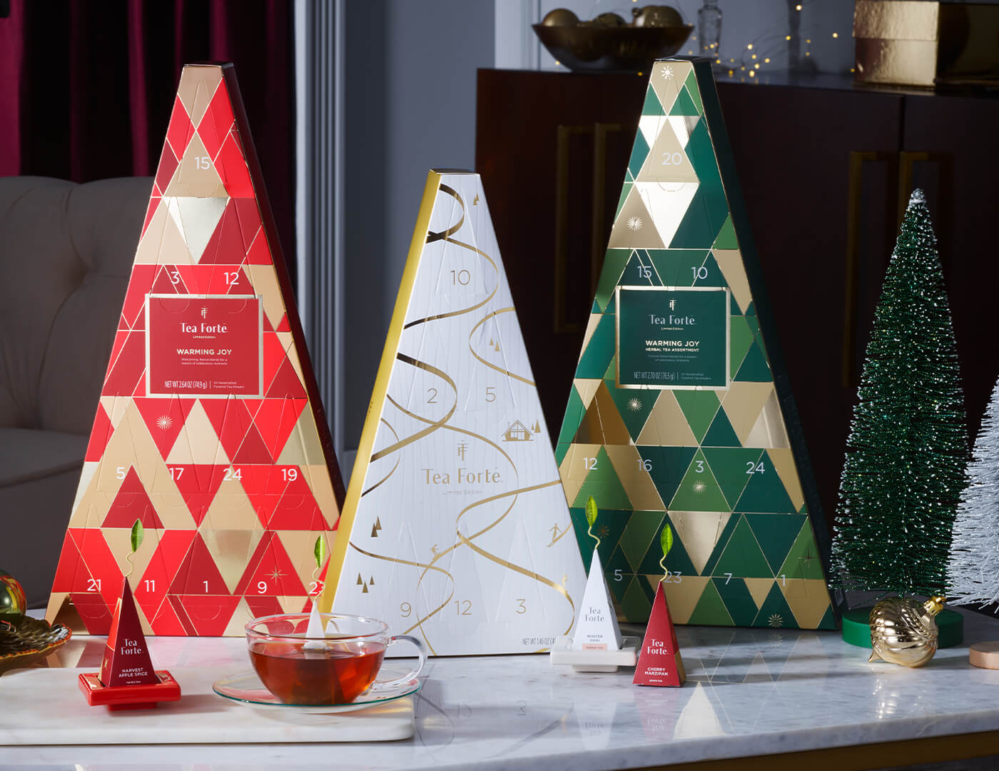 Trio of Trees Advent Calendars, one of each: Warming JOy Assorted Advent, Warming Joy Herbal Advent and Winter Chalet 12 days of cozy teas advent on a table with winter decorations