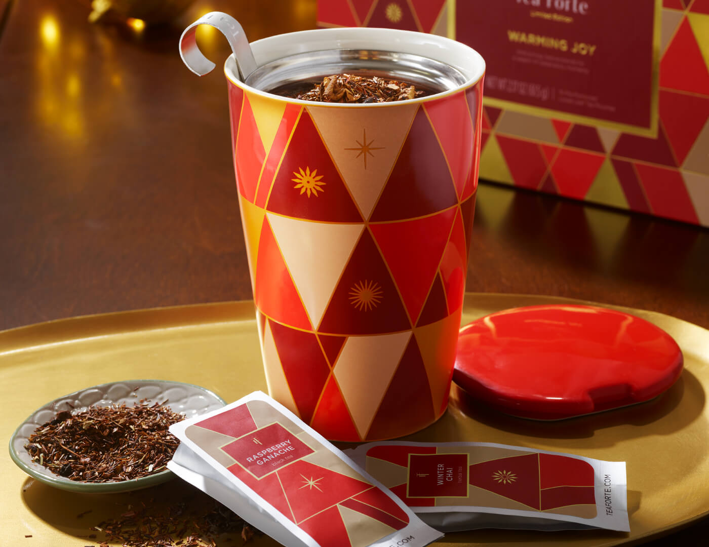 Warming Joy KATI Steeping Cup with infuser and loose tea inside, cover off, on a gold tray with single steeps pouches