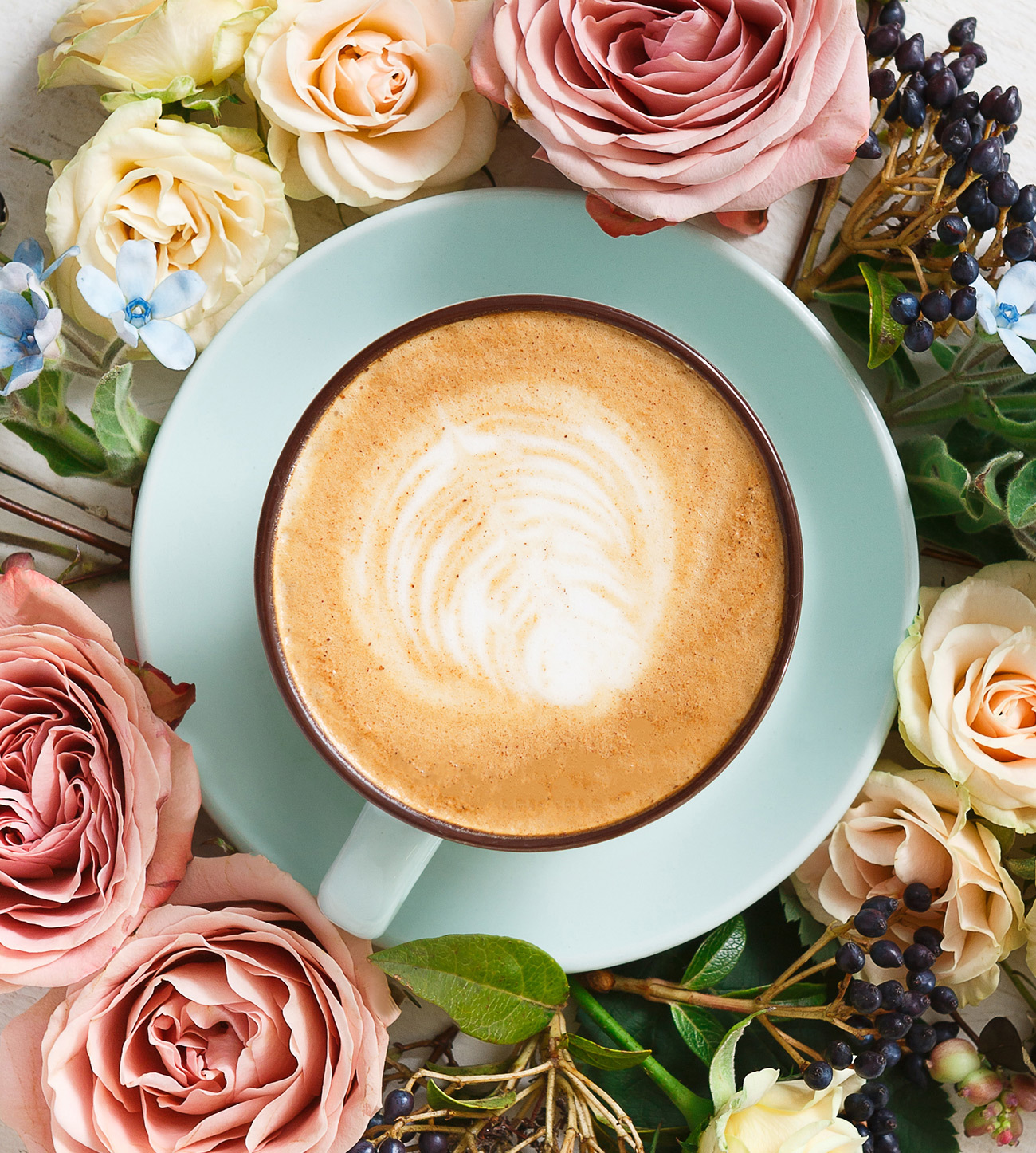 Pumpkin Spice Latte in a decorative light blue cup and saucer surrounded with roses in pink and off white