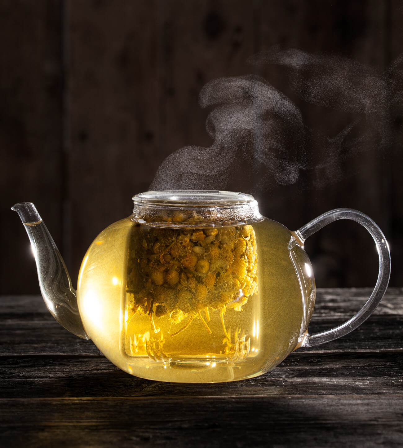 Steeping herbal tea in a glass teapot on a dark background