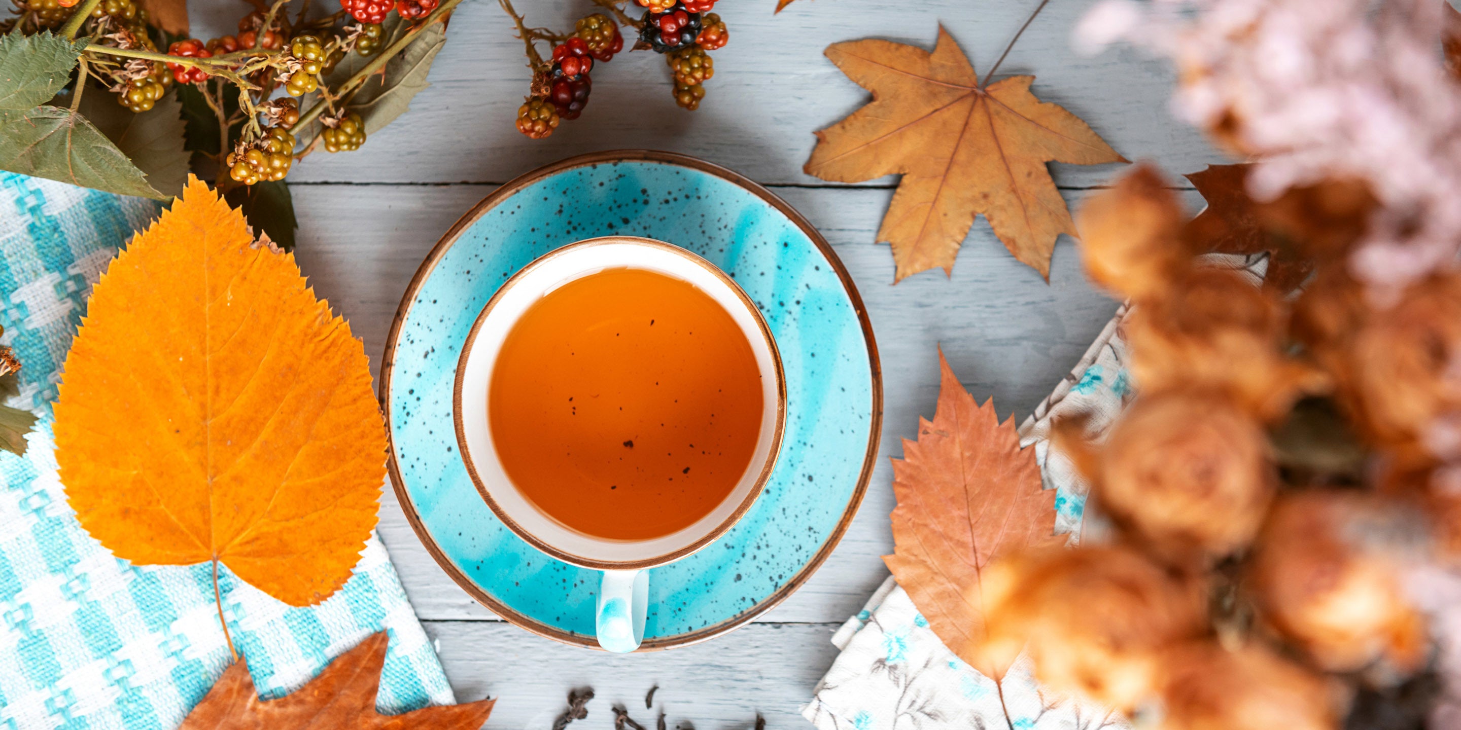 Cup and saucer of orange tea with autumn leaves surrounding it