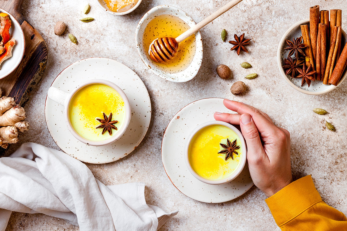 Table with teacups of Turmeric Tantra Chai Golden Milk, honey and spices